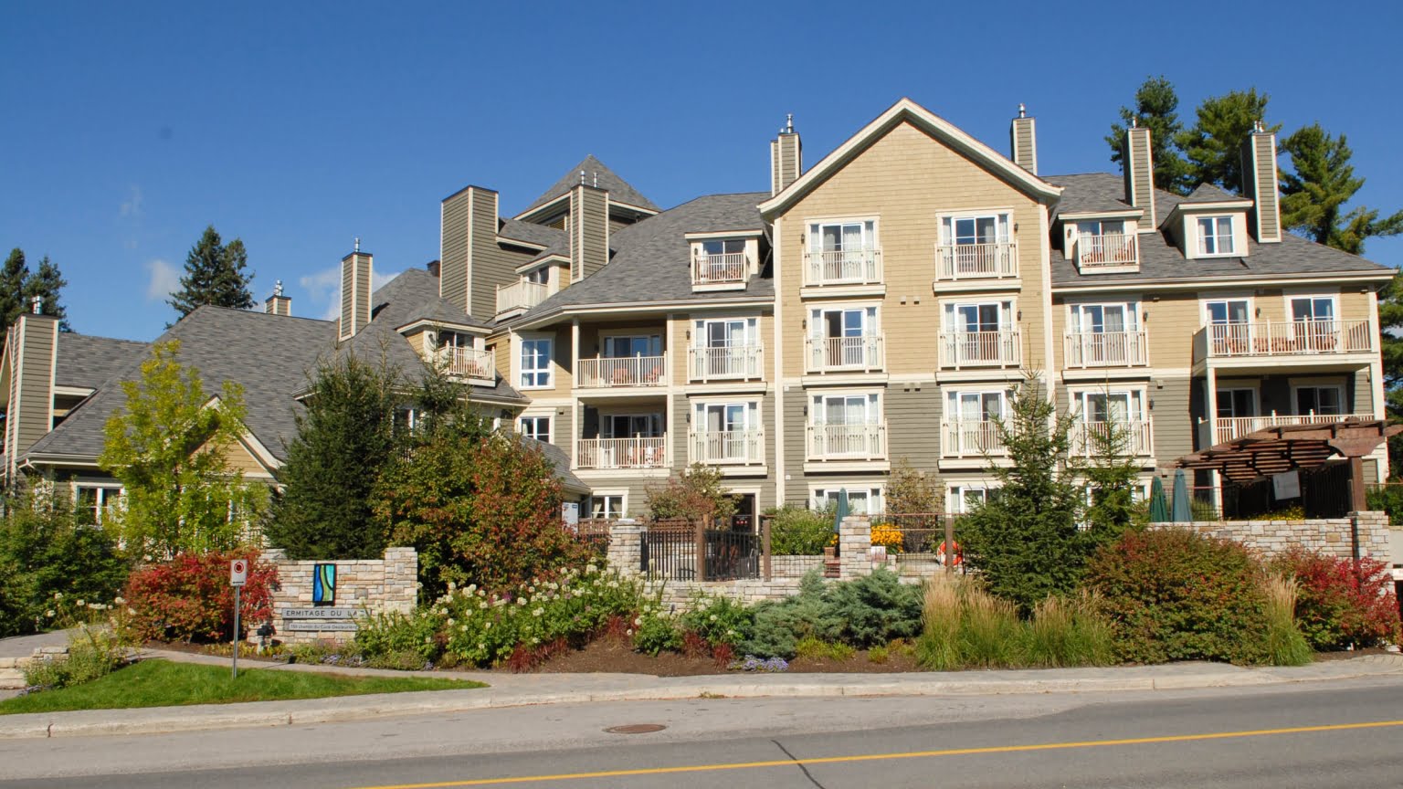 Ermitage du Lac Boutique hotel exterior of Ermitage du Lac on a sunny summer day, showcasing the luxury condo buildings with private balconies and manicured landscaping under a blue sky at Mont Tremblant Pedestrian Village, Quebec.