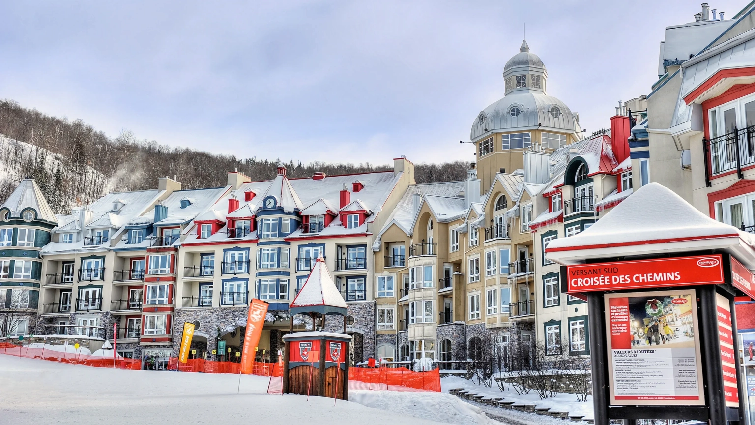 sommet-des-neiges-winter Alpine hotel exterior and architecture of Sommet des Neiges on a snowy winter day, highlighting the colorful resort buildings and a red sign reading "VERSANT SUD CROISÉE DES CHEMINS" in Mont-Tremblant, Quebec.